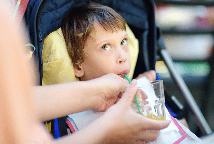 Young girl drinking from a cup and straw being held for her by a carer.